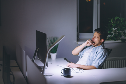 Man working late yawning in front of a computer