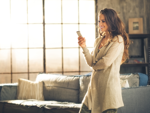 Woman standing and changing channel on tv at home