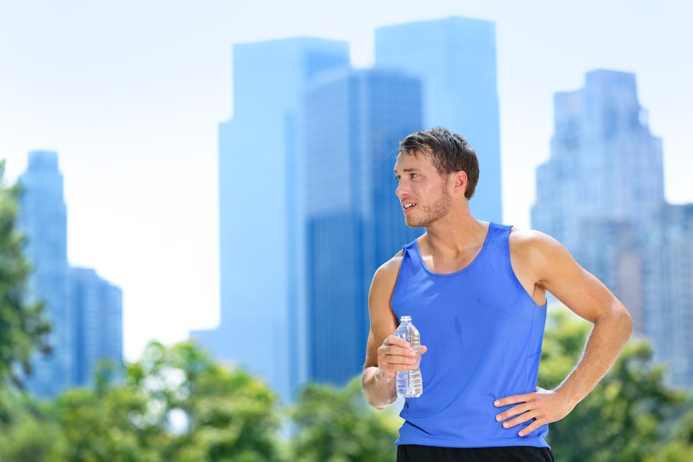 Man drinking water bottle during hot summer exercise