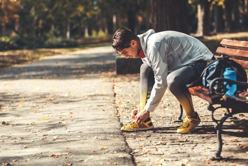 Man tying shoes on a park bench during walk
