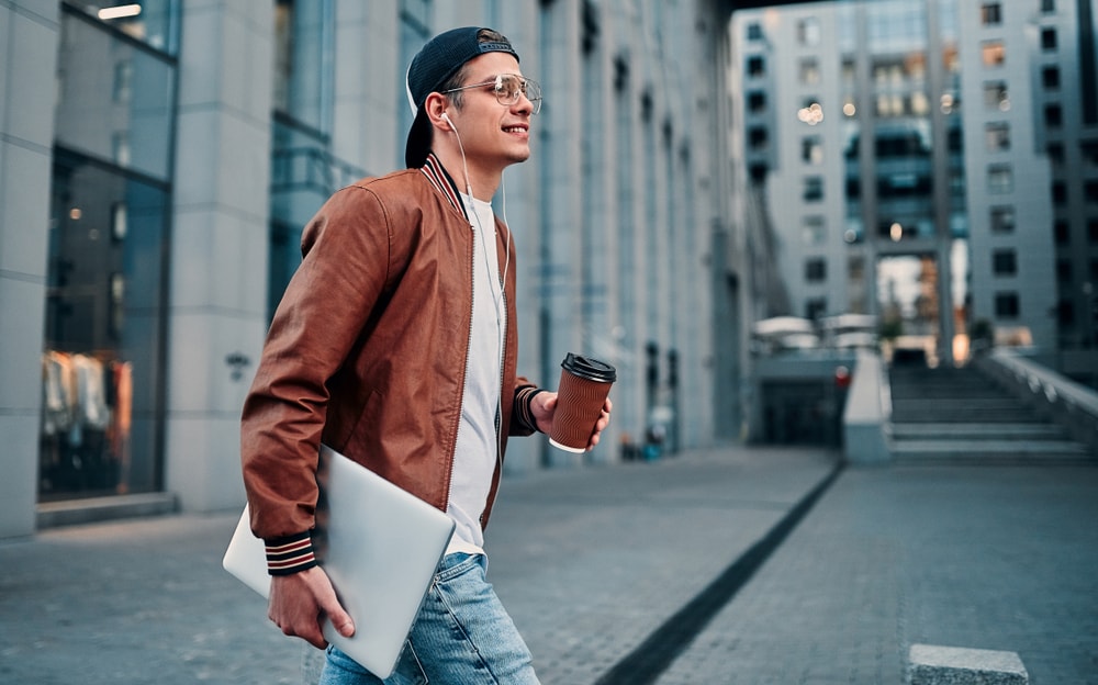 Young man with computer crossing the street