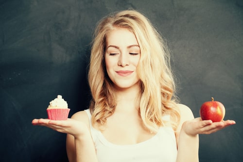 Woman choosing between cupcake and apple