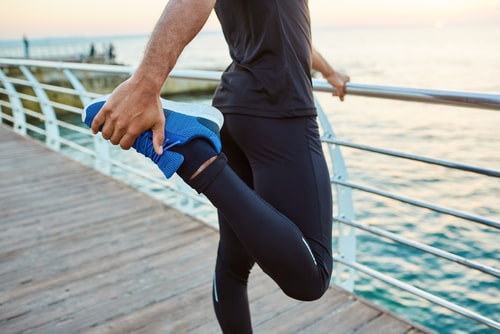 Jogger stretching thighs on a bridge over water