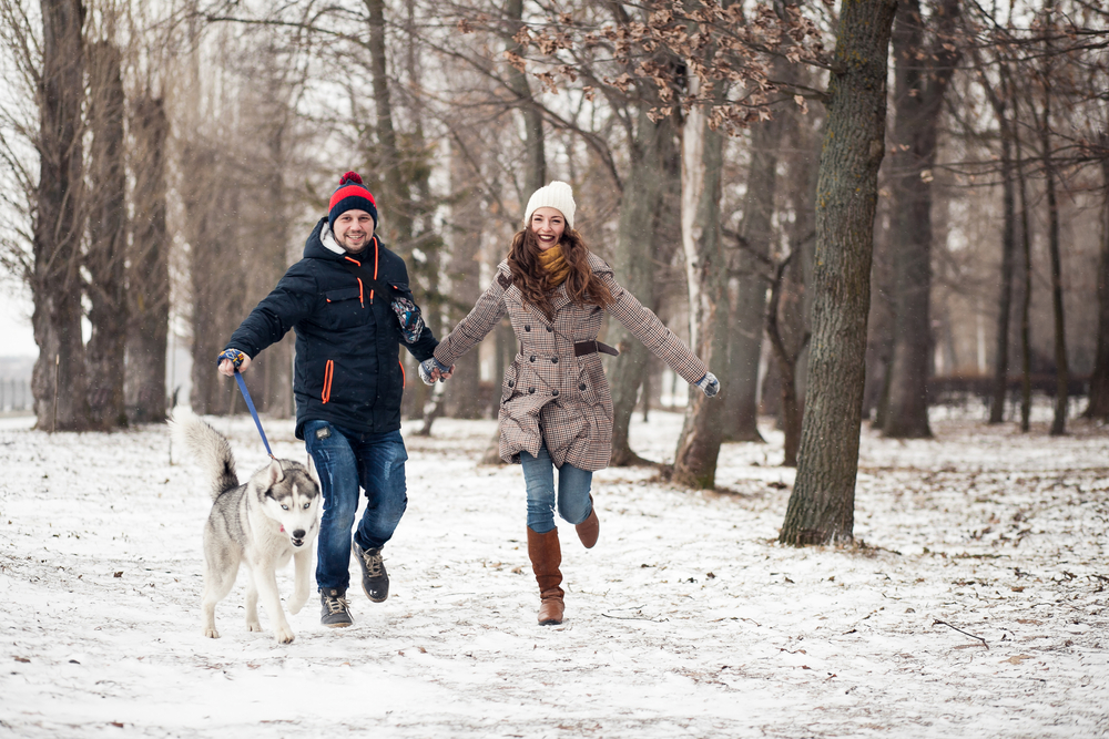 Couple having fun walking dog in winter snow