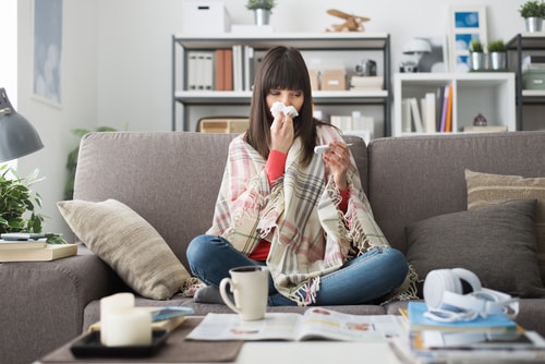 Sick woman sitting on couch reading thermometer