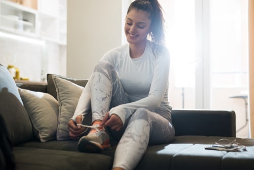 Woman sitting on couch tying shoes to go for a walk