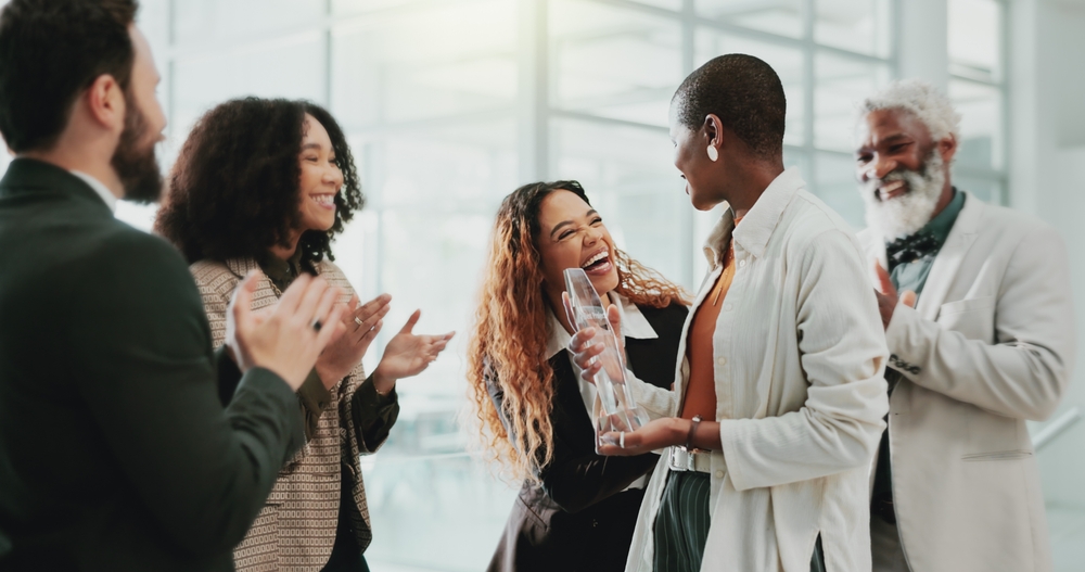 A team lead handing a step challenge prize to a smiling employee while coworkers applaud