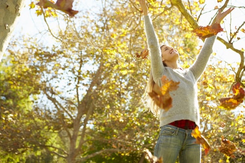 Happy woman throwing leaves in autumn