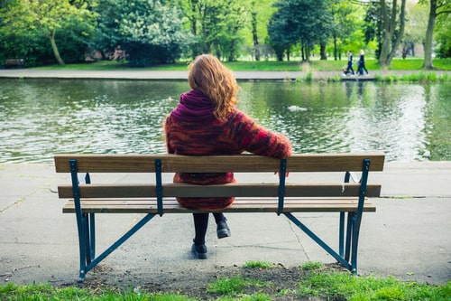 Woman sitting on park bench in front of lake