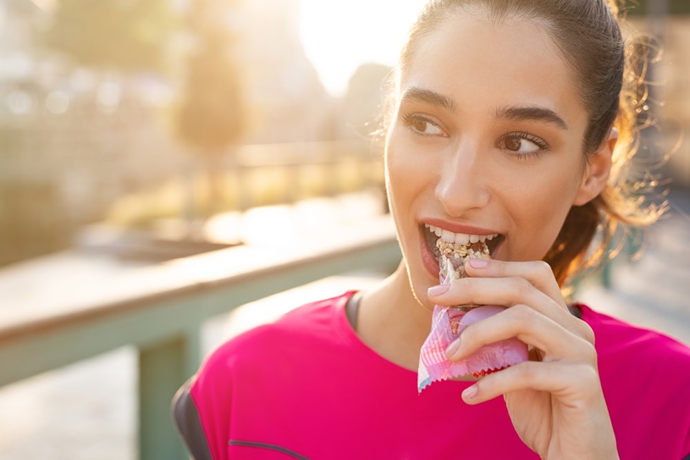 Athletic woman eating an energy bar outside